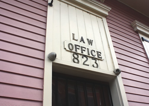 A close-up view of an exterior building wall with horizontal paneling painted in a soft pink color. The central focus is a large rectangular plaque stating 'LAW OFFICE 823' in bold letters. The paneling and design suggest a historical or vintage style.