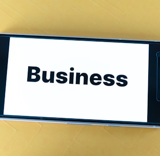 A smartphone lying on a yellow surface displays the word 'Business' in bold black text on its screen.